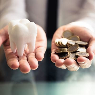 Hand with a model tooth and another hand with coins
