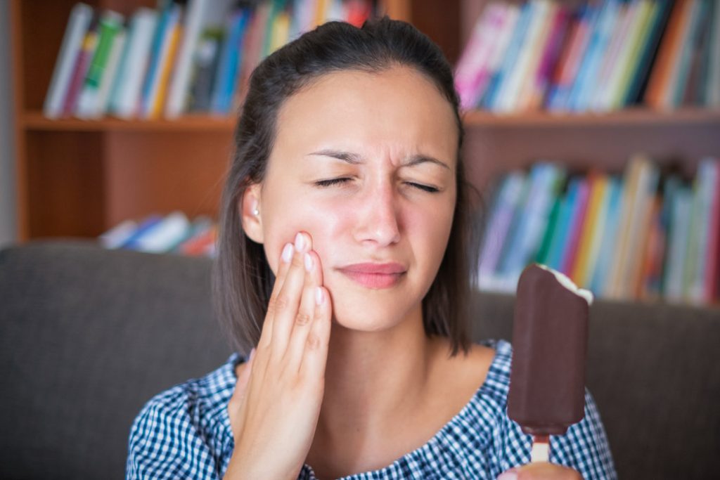 Woman with sensitive teeth recoils in pain after eating ice cream.