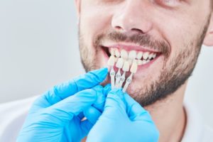 cosmetic dentist holding a row of veneers up to a patient’s smile 