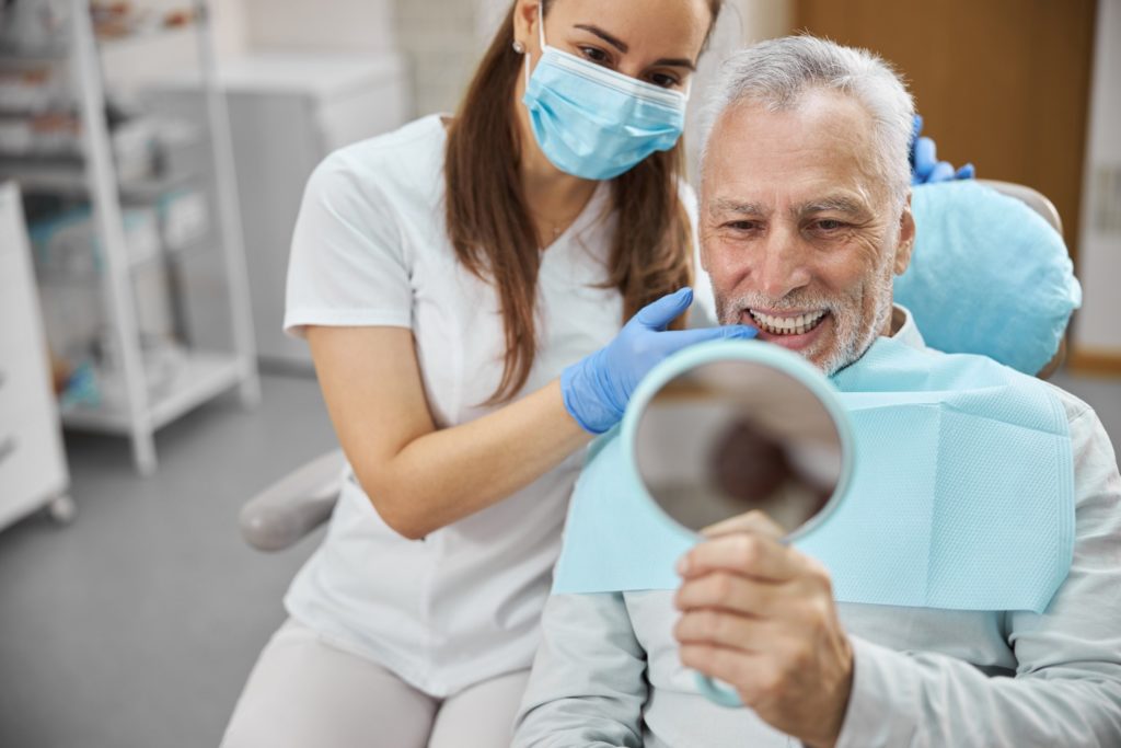 Patient with dental implants smiling in dentist's mirror