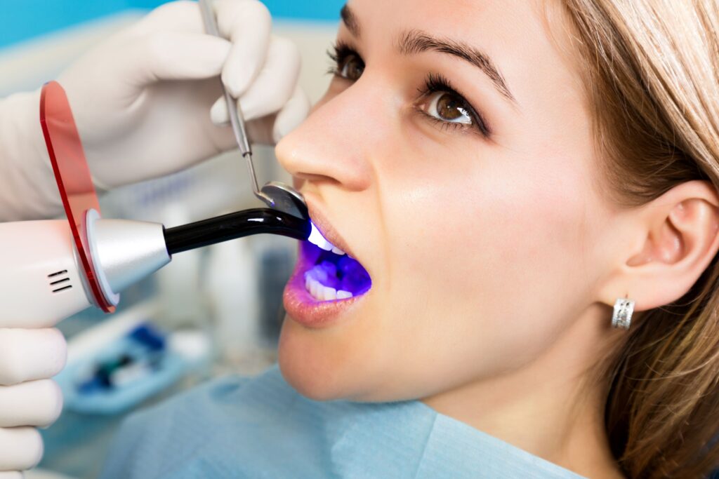 Dentist using UV light to harden woman's dental filling