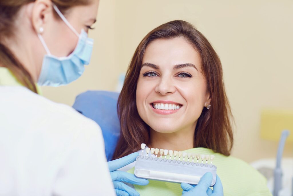 Woman smiling with dentist holding shade guide close to her teeth