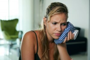 Woman holding ice pack to her face in pain.