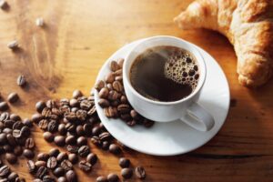 Steaming cup of coffee with coffee beans and bagel nearby.
